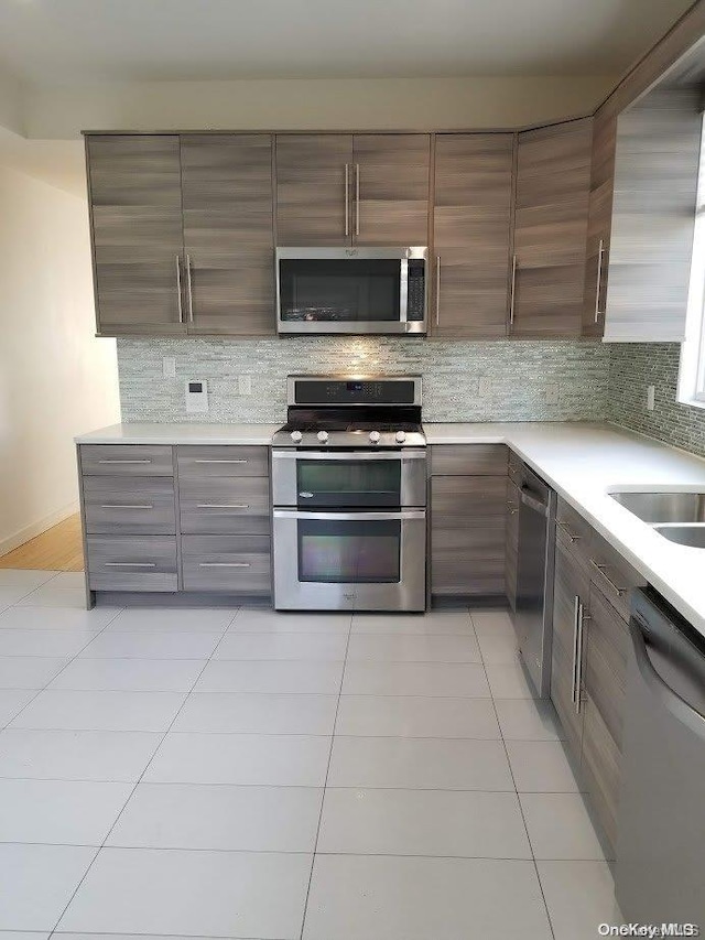 kitchen with backsplash, sink, light tile patterned floors, and stainless steel appliances