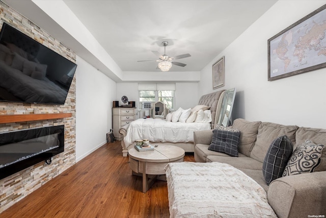 bedroom featuring ceiling fan, a stone fireplace, and wood-type flooring