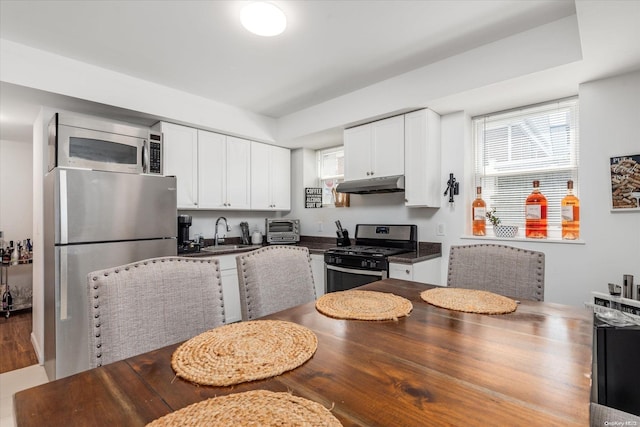 525 Bch 138th St Unit A2, Belle Harbor, NY 11694 - kitchen featuring stainless steel appliances, under cabinet range hood, a sink, dark countertops, and white cabinets