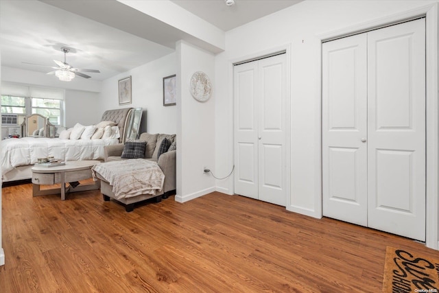 bedroom with ceiling fan, wood-type flooring, and two closets