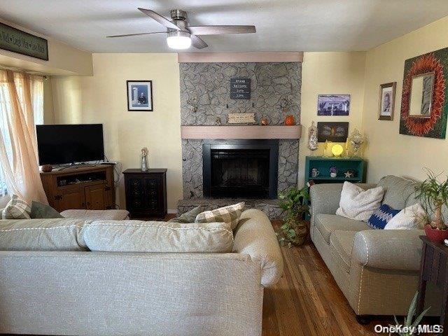 living room with ceiling fan, a stone fireplace, and dark hardwood / wood-style flooring