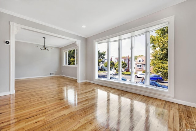 spare room with light wood-type flooring, an inviting chandelier, and ornamental molding