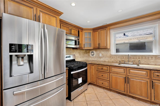 kitchen with light stone countertops, sink, backsplash, light tile patterned flooring, and appliances with stainless steel finishes