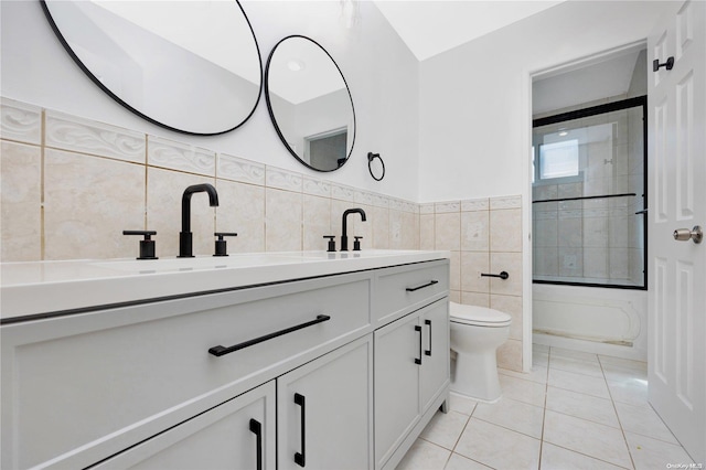 full bathroom with combined bath / shower with glass door, vanity, tile walls, tile patterned flooring, and toilet