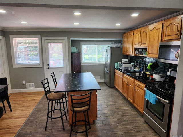 kitchen with appliances with stainless steel finishes, dark hardwood / wood-style flooring, backsplash, a breakfast bar, and sink