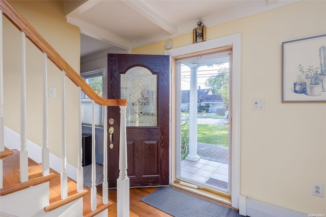 entryway with wood-type flooring, ornamental molding, and beam ceiling