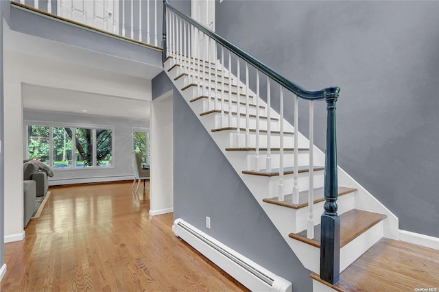 stairs with baseboards, wood finished floors, a high ceiling, baseboard heating, and a baseboard heating unit