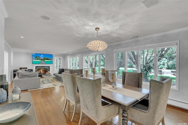 dining space with crown molding, a glass covered fireplace, visible vents, and light wood-style floors