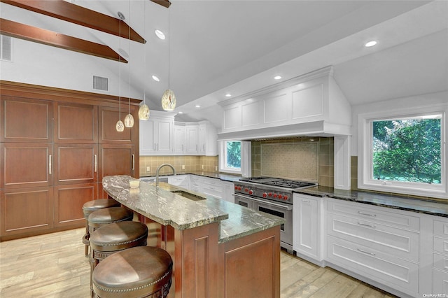 kitchen featuring visible vents, range with two ovens, dark stone countertops, vaulted ceiling with beams, and a sink