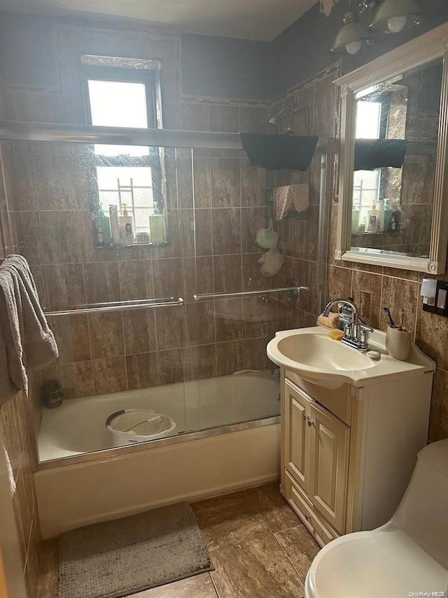 full bathroom featuring vanity, a healthy amount of sunlight, combined bath / shower with glass door, and tile walls