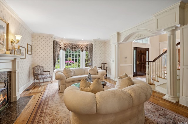 living room featuring ornate columns, light wood-type flooring, a fireplace, and ornamental molding