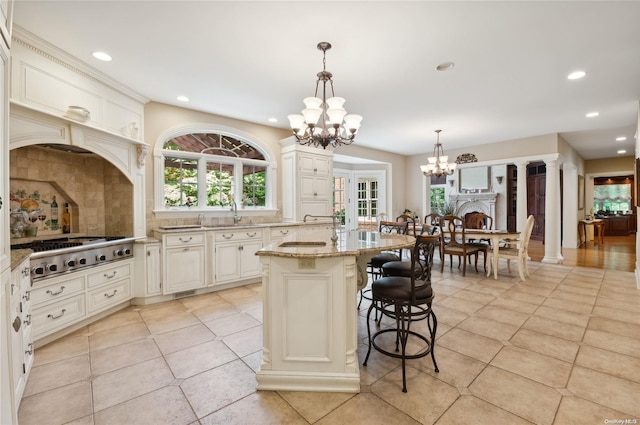 kitchen with light stone countertops, a kitchen breakfast bar, pendant lighting, stainless steel gas stovetop, and a kitchen island with sink