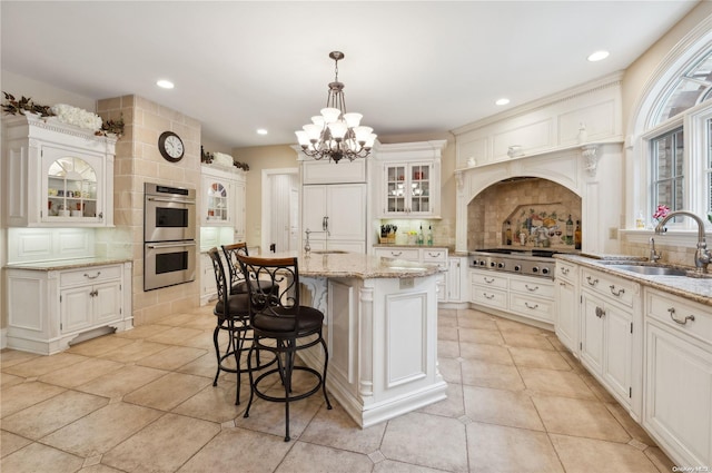 kitchen with a kitchen island with sink, sink, decorative backsplash, appliances with stainless steel finishes, and decorative light fixtures