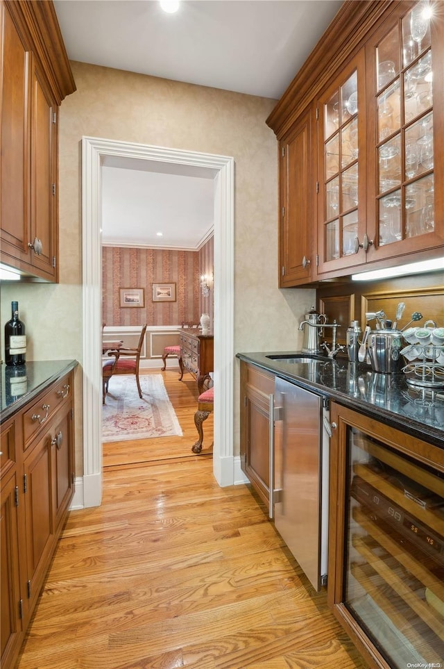 bar with stainless steel fridge, dark stone counters, beverage cooler, sink, and light hardwood / wood-style flooring