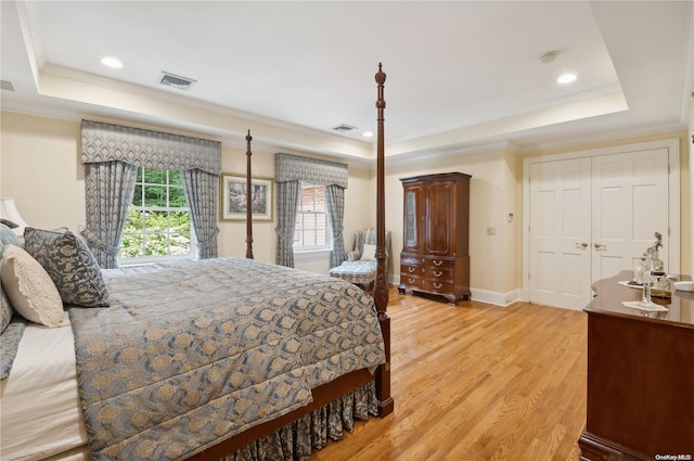 bedroom featuring light hardwood / wood-style flooring, a tray ceiling, and multiple windows