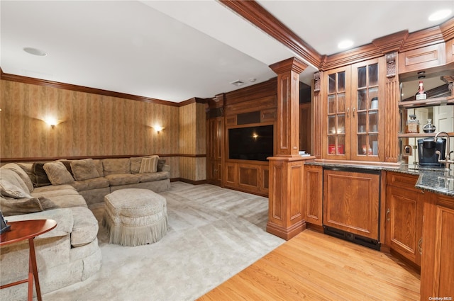 living room featuring light wood-type flooring, crown molding, wooden walls, and ornate columns