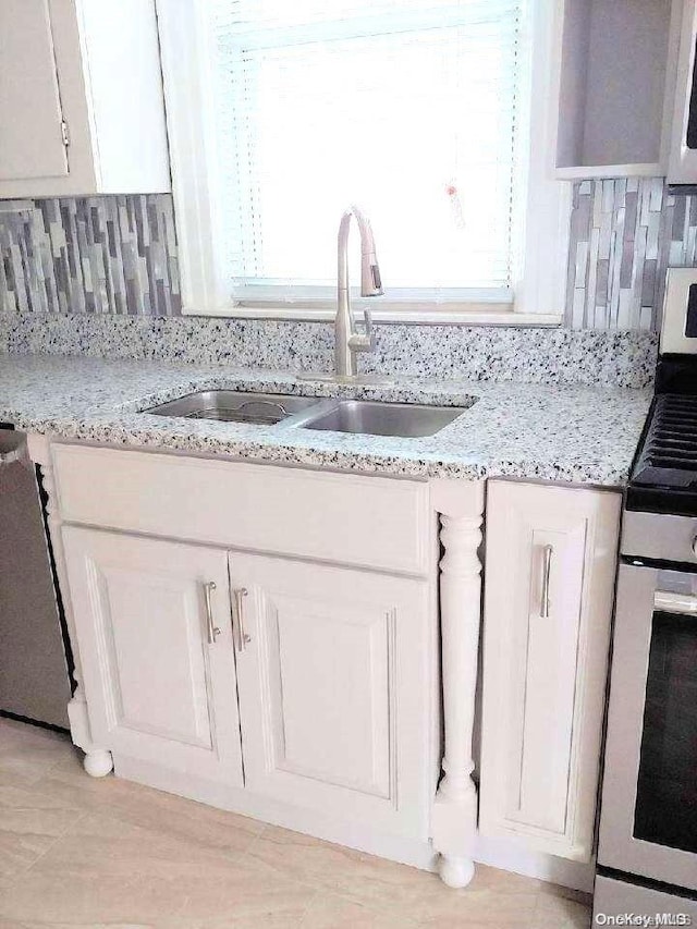 interior details featuring decorative backsplash, appliances with stainless steel finishes, light stone countertops, sink, and white cabinets