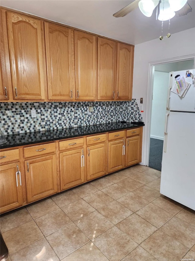 kitchen with decorative backsplash, white refrigerator, dark stone countertops, and light tile patterned floors