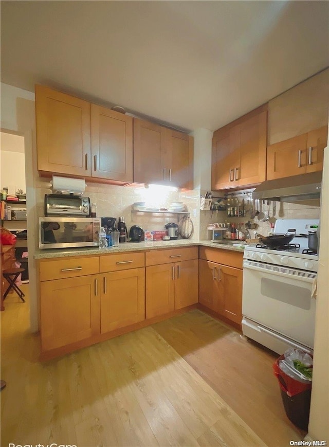 kitchen with white gas stove, light hardwood / wood-style floors, decorative backsplash, and light brown cabinetry