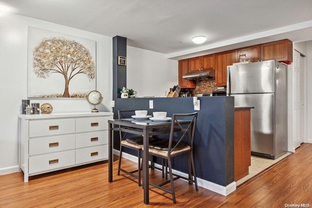 kitchen featuring white cabinets, decorative backsplash, light wood-type flooring, and stainless steel refrigerator