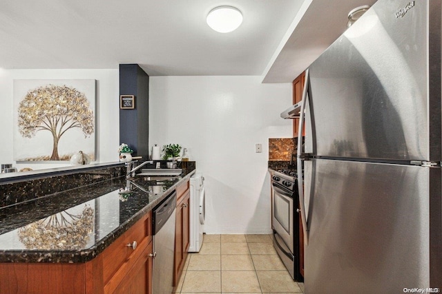 kitchen featuring dark stone counters, stainless steel appliances, sink, light tile patterned floors, and washer / clothes dryer