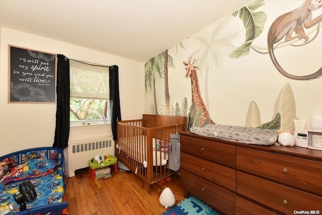 bedroom featuring radiator heating unit, a nursery area, and hardwood / wood-style flooring