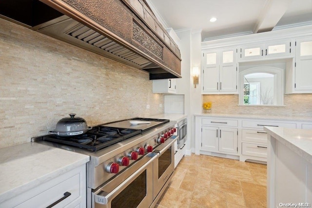 kitchen with backsplash, premium range hood, range with two ovens, ornamental molding, and white cabinetry