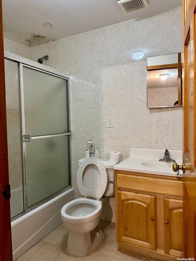 full bathroom featuring tile patterned flooring, combined bath / shower with glass door, toilet, vanity, and tile walls