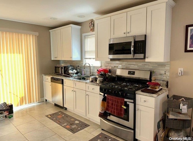 kitchen featuring tasteful backsplash, stainless steel appliances, sink, light tile patterned floors, and white cabinets