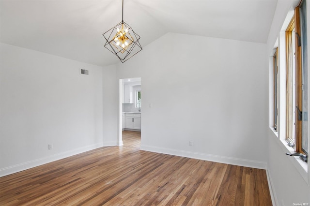 empty room with hardwood / wood-style flooring, a notable chandelier, and lofted ceiling