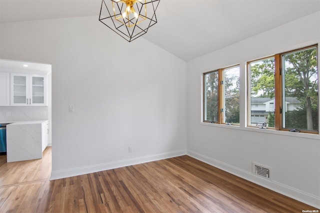 spare room featuring an inviting chandelier, light hardwood / wood-style flooring, and vaulted ceiling