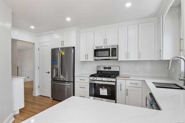 kitchen with white cabinetry, sink, stainless steel appliances, light stone counters, and light hardwood / wood-style flooring