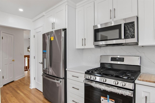 kitchen featuring backsplash, white cabinetry, light wood-type flooring, and appliances with stainless steel finishes