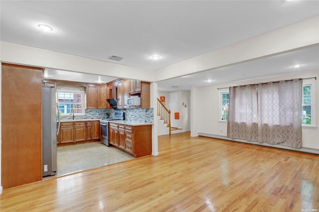 kitchen with decorative backsplash, appliances with stainless steel finishes, a baseboard heating unit, sink, and light hardwood / wood-style flooring