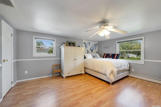 bedroom featuring light hardwood / wood-style flooring, multiple windows, a baseboard heating unit, and ceiling fan