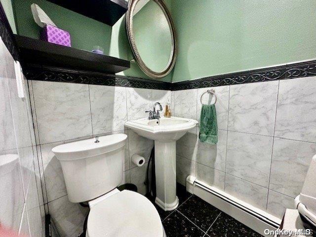 bathroom with toilet, baseboard heating, and tile walls