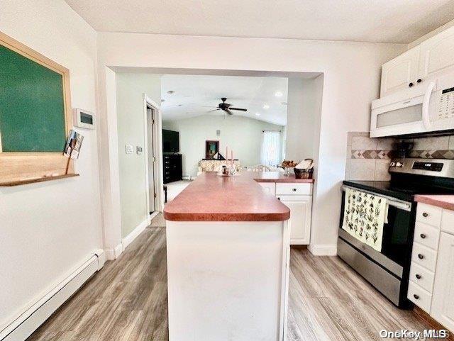 kitchen featuring lofted ceiling, white cabinetry, stainless steel electric range oven, and a baseboard heating unit