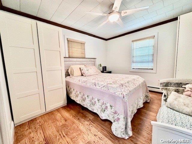 bedroom featuring ceiling fan, ornamental molding, baseboard heating, and light hardwood / wood-style flooring