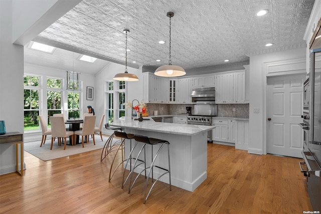 kitchen featuring pendant lighting, white cabinets, sink, stainless steel stove, and light hardwood / wood-style flooring