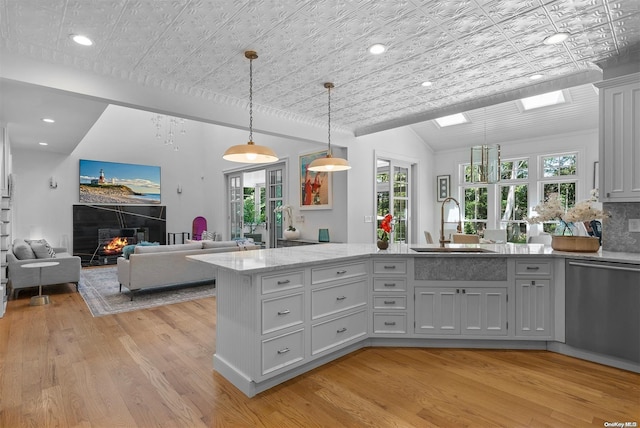 kitchen featuring dishwasher, light wood-type flooring, sink, and decorative light fixtures