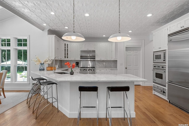 kitchen with built in appliances, decorative light fixtures, white cabinetry, and lofted ceiling