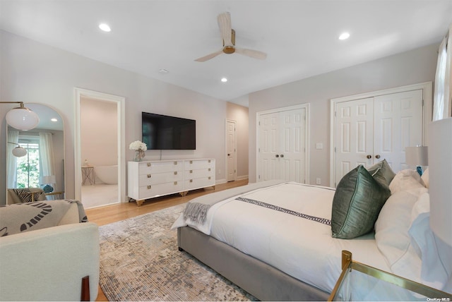 bedroom featuring ensuite bathroom, ceiling fan, two closets, and light wood-type flooring