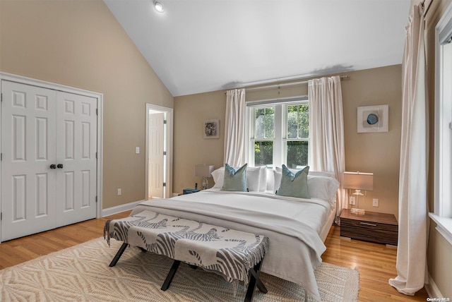 bedroom featuring high vaulted ceiling, light hardwood / wood-style flooring, and a closet