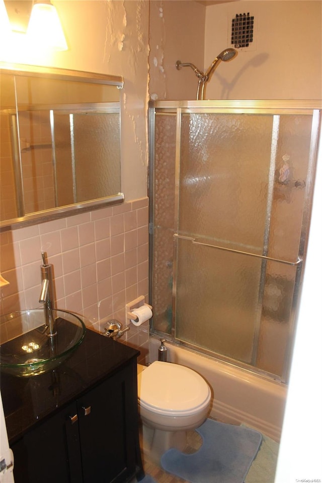 full bathroom with tile walls, vanity, bath / shower combo with glass door, and toilet