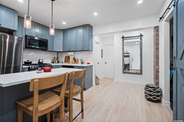 kitchen featuring a breakfast bar, a barn door, light wood-type flooring, appliances with stainless steel finishes, and tasteful backsplash