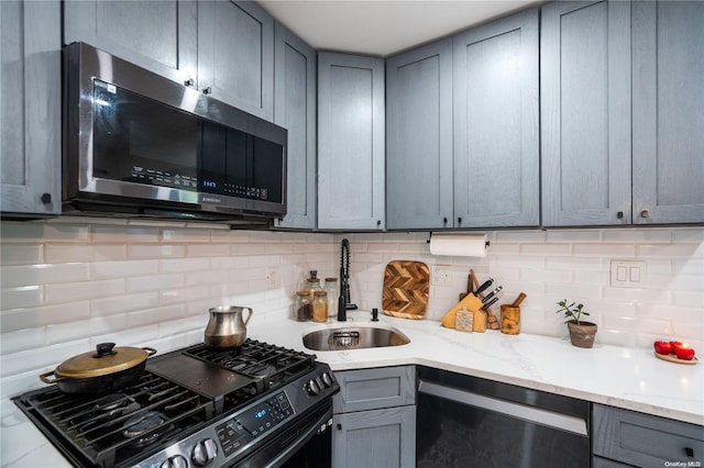 kitchen featuring stainless steel appliances, light stone counters, tasteful backsplash, and sink