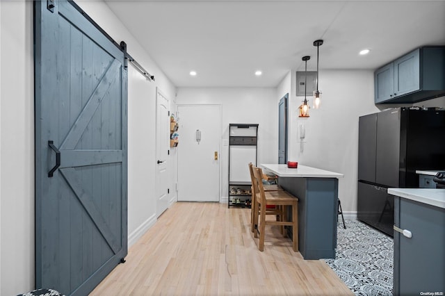 kitchen with a breakfast bar, black fridge, hanging light fixtures, a barn door, and light wood-type flooring