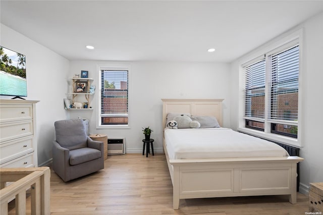 bedroom with multiple windows, heating unit, and light wood-type flooring