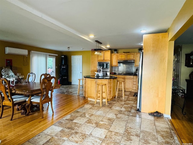 kitchen featuring a wall mounted air conditioner, light hardwood / wood-style flooring, a kitchen bar, a kitchen island, and appliances with stainless steel finishes