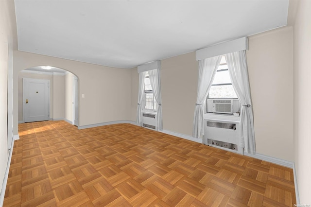 empty room with cooling unit, radiator heating unit, a healthy amount of sunlight, and light parquet floors